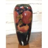 A tall tapering Moorcroft vase embossed with tube-lined vines and pomegranates on dark glazed ground