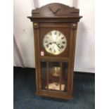 A 1930s stained wallclock, the arched crest with applied moulding above a glazed door with