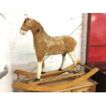 A pony-skin covered rocking horse with glass eyes and wood handles, raised on shaped rocking