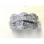 A 9ct white gold dress ring, the scalloped panel pave set with diamonds having central waved band