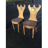 A pair of early nineteenth century mahogany hall chairs with crescent scroll carved backs centred by