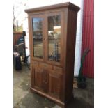 A glazed stained cabinet with moulded cornice above a pair of glazed doors enclosing shelves, having