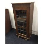 An oak cupboard with chisel carved top and fluted frieze above a leaded glass door enclosing