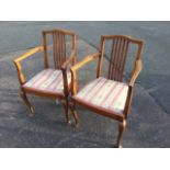 A pair of mahogany armchairs with arched slatted backs and tapering arms above upholstered webbed
