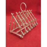 A silver plated rifle toast rack, the six divisions framed by crossed guns, raised on rectangular