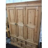 A pine wardrobe with moulded cornice above three panelled doors enclosing hanging space, the base