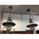 A pair of industrial style metal hanging lights with flared shades hung from chains and ceiling