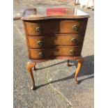 A 50s serpentine fronted walnut cabinet of three drawers, the moulded top with carved edge, the