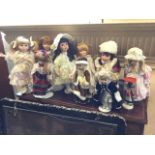 A collection of eight porcelain head girl dolls on stands - wedding dressed, nighties, Christmas,