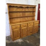 A reproduction pine dresser, with moulded cornice above a waved apron and two plate shelves with