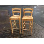 A pair of beech high stools, with curved back rails above rush seats, raised on rectangular legs
