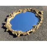 An oval gilt mirror in rococo scrolled plaster frame having floral mounts. (20in x 27in ext)