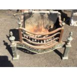 A dog grate having burning basket with bowfronted bars framed by brass urn finials, above a