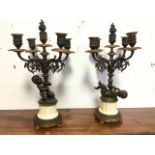 A pair of bronze candelabra each with putti supporting five urn shaped candleholders with acanthus