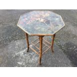 An octagonal burnt bamboo lamp table, the lacquered tray top with bird decoration raised on cane