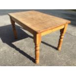 A rectangular pine kitchen table with thick plank top raised on turned column legs. (54in x 33in x