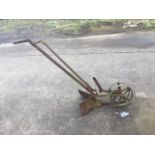 An antique plough with twin spoked wheels leading a flared arrow shaped blade, the angled handles