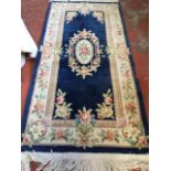 A Chinese thick pile wool rug woven with oval floral medallion on blue field framed by ivory