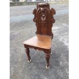 A Victorian oak hall chair with scroll carved panelled back centered by pierced roundel with shield,
