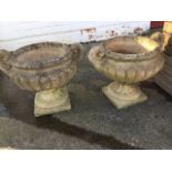 A pair of composition stone urns, the fluted pots with scroll moulded handles having tubular rims,