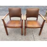 A pair of oak armchairs with brass studded upholstered backs and chamfered arms above drop-in seats,