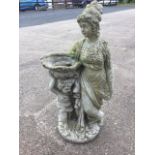 A composition stone birdbath cast as a mother & child supporting bowl amongst drapery, raised on