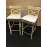 A pair of painted high stools with curved back rails above crossed slats, having cushion seats
