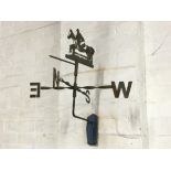 A wrought iron weather vane with compass points on twisted bars beneath a pointer mounted with