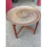 A circular embossed copper coffee table, the tray decorated with leaf designs having ribbed border