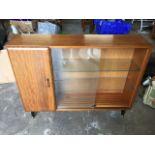 A 1960s Turnidge teak side cabinet with sliding glass doors beside a cupboard, raised on angled