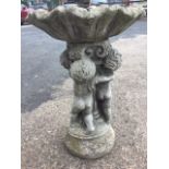 A composition stone birdbath with scalloped bowl supported by three cherubs on circular moulded