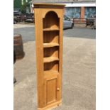 A reproduction pine corner cupboard with moulded cornice above an arched apron and three open shaped