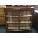 A bowfronted walnut display cabinet, the moulded top with shaped upstand above a pair of astragal