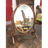 An oval mahogany dressing table mirror, the bevelled plate in cushion moulded frame, raised on