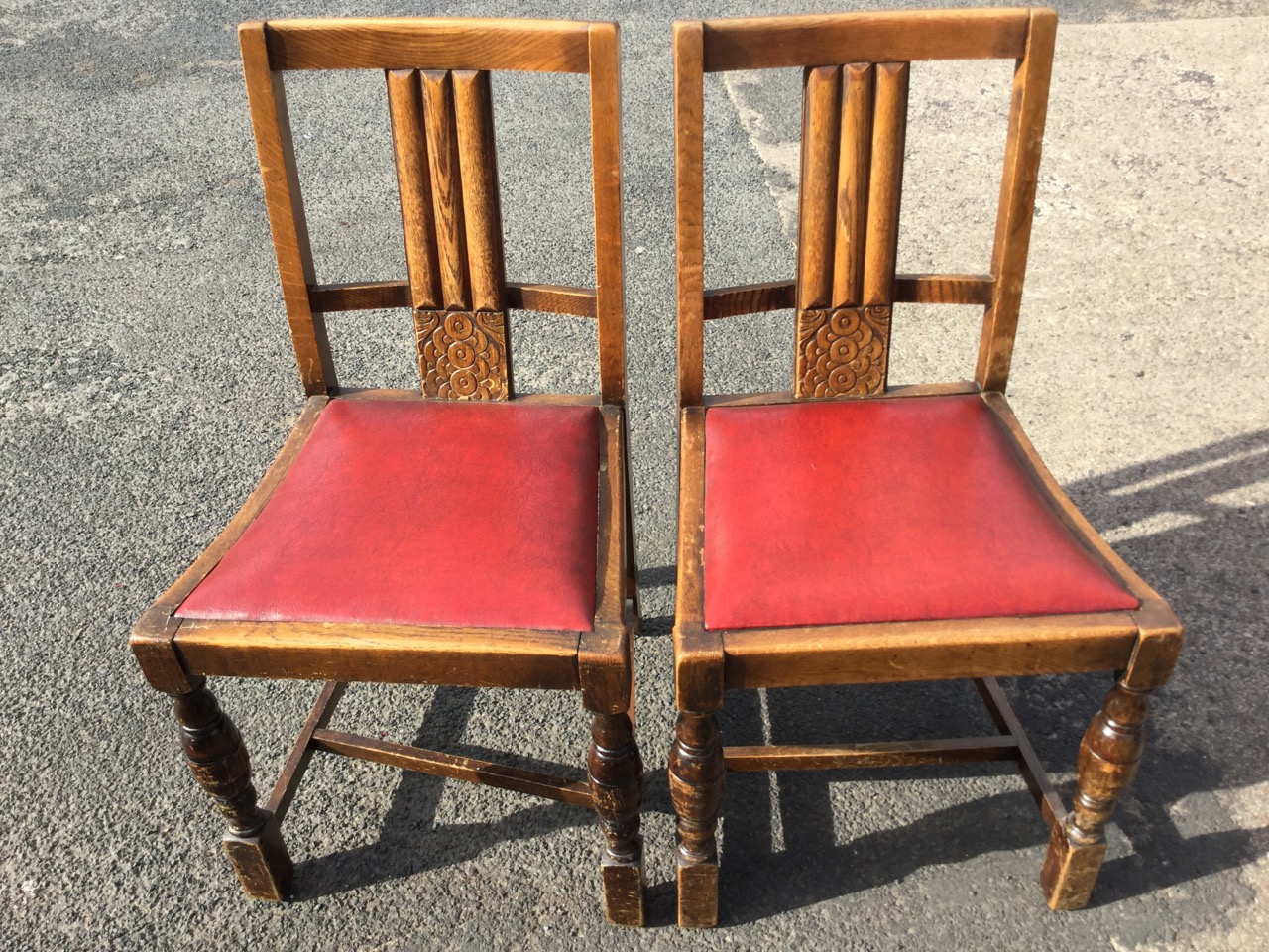 A pair of 1930s oak chairs with fluted splats above stylised carved roundel panels, the drop-in