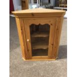 A pine corner cabinet with moulded cornice above a glazed door enclosing shaped shelves, framed by