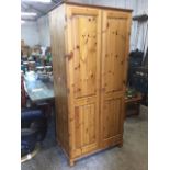 A pine wardrobe with two fielded panelled doors enclosing hanging space, raised on bun feet. (34.5in