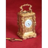 A miniature gilt metal carriage clock with caryatid corners to case framing foliate scrolled panels,