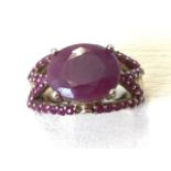 A large silver gilt ruby ring, set with oval claw mounted stone above lines of smaller stones,