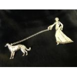 A deco style silver brooch in two parts, with elegant lady walking her hound on chain, her robe