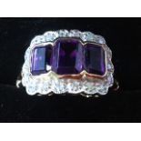 A 9 carat gold ring set with three emerald cut amethysts, the rectangular panel having scalloped