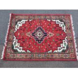 An Indo-Hamadan wool rug woven with ink blue stepped medallion on floral red field, the spandrels in