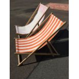 A pair of folding beech deck chairs, each with striped canvas seats - one faded. (2)