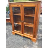 A rectangular glazed pine bookcase cabinet, the moulded top above a press moulded frieze, having