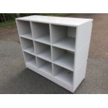 A rectangular storage unit with nine compartments on plinth, raised on casters. (47.25in x 17.75in x