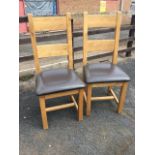 A pair of modern oak dining chairs with plain backs above padded leather seats, raised on square