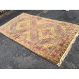 A Turkish rug woven with twin flowerhead medallions in waved bands of mauve, grey and mustard, the