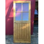 A glazed pine tongue & grooved door with four panes above a boarded panel, mounted with brass door