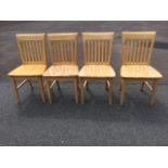 A set of four hardwood kitchen chairs with slatbacks above wide solid seats, raised on square