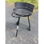 An unused barbecue stand with adjustable chromed grill above circular fire bowl, raised on three